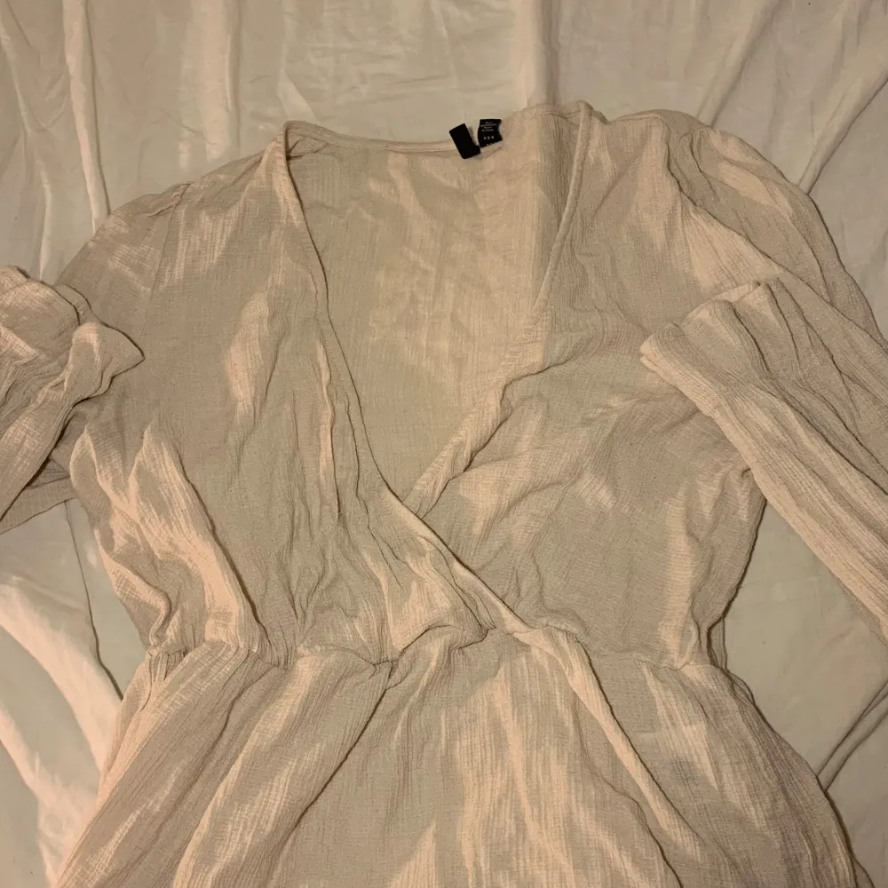 Säljer en stilren beige omlottklänning från Vero Moda. Klänningen har en v-ringad design och långa ärmar, perfekt för en elegant look. Materialet är mjukt och bekvämt, vilket gör den idealisk för både vardag och speciella tillfällen.. Puserot.
