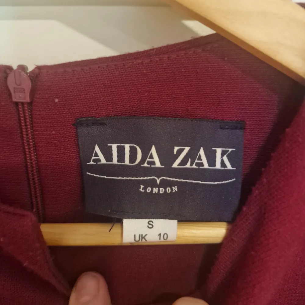 Snygg vinröd klänning från Aida Zak med kort ärm och en elegant passform. Klänningen har en liten öppning med knappar i nacken och en diskret dragkedja i ryggen. Super bekväm tyget har börjat noppa sig lite, tyvärr.. Mekot.