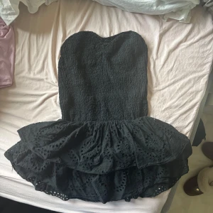 Svart axelbandslös klänning - Snygg svart axelbandslös klänning med volangdetaljer och broderad nederdel. Perfekt för en kväll ute eller en speciell tillställning. Klänningen har en kort längd och en smickrande passform. Storlek M men passar även mig som har xs då den är väldigt stretchig. Nästan identisk till den från meet me there!  ❤️