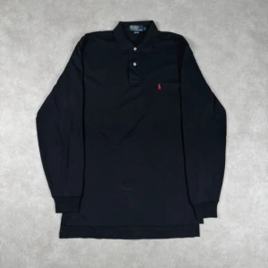 Svart långärmad pikétröja från Polo Ralph Lauren - Säljer en klassisk svart långärmad pikétröja från Polo Ralph Lauren med den ikoniska röda loggan på bröstet. Tröjan har en krage med knappar och är perfekt för en stilren look. Tröjan är M men är stor i storleken så rekommenderar för L. Pris kan spklart diskuteras