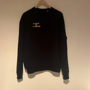 D’once de la sense Sweatshirt  - Säljer en marinblå tröja med texten 'D'ONCE DE LA SENSE' i gult på bröstet. Tröjan har långa ärmar och en rund halsringning. Perfekt för en stilren och avslappnad look. Använd max 3 gånger. Har endast legat i en garderob ett tag och aldrig kommit till användning 