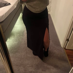 Svart långkjol med slits - Snygg svart långkjol med en stilren slits på sidan. Perfekt för att ge en elegant touch till din outfit. Kjolen har en klassisk passform och är lätt att matcha med olika toppar.