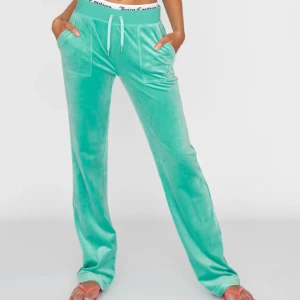 Turkosa mjukisbyxor från Juicy Couture - Snygga turkosa mjukisbyxor från Juicy Couture i mjukt material. Byxorna har en elastisk midja med snörning och praktiska fickor fram och bak. Perfekta för en avslappnad stil.