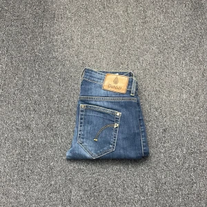 Dondup jeans - Snygga blå jeans från Dondup med klassisk femficksdesign och kontrasterande gul söm. De har en läderpatch med logotyp baktill i midjan. Perfekta för en stilren look.