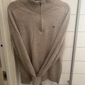 Beige merinoulltröja från Morris - Säljer en stilren beige tröja från Morris i 100% merinoull. Tröjan har en dragkedja vid halsen och en liten broderad logotyp på bröstet. Perfekt för kyligare dagar med sin mjuka och varma känsla.