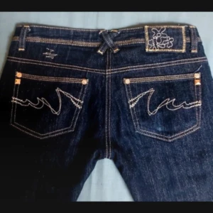 Mörkblå bootcut jeans med broderade fickor - Snygga mörkblå bootcut jeans med broderade detaljer på bakfickorna. Sista bilden är min, de andra tillhör den tidigare ägaren. Skriv för fler bilder!    Innerbenslängd: 81 cm                                             Midjevidd: 37 cm