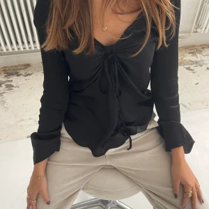 Svart blus med knyt och volangdetaljer - Blus från design by si. Aldrig använd. Prislappen sitter kvar. Köpt för 408kr 