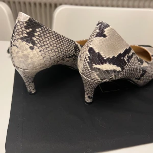 Ormmönstrade pumps från Stinaa.J - Snygga ormmönstrade pumps från Stinaa.J i skinn. Skorna har en spetsig tå och en elegant klack, perfekt för att ge en stilfull touch till din outfit.. Använda en gång, säljer pga fel modell för mina fötter. Inköpt för nypris 4000 kr. 
