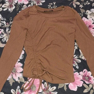 Brun ribbad tröja med snörning - Säljer en brun ribbad tröja med lång ärm och snygg snörningsdetalj på sidan. Perfekt för en trendig look. Passar bra till både jeans och kjol. Hör av dig vid intresse!