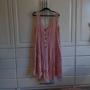 Rosa ärmlös klänning med knappar - Charmig rosa klänning med ett lätt och luftigt tyg. Den har en ärmlös design och knappar framtill som ger en söt touch. Perfekt för varma dagar och avslappnade tillfällen.