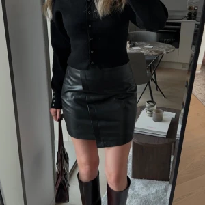 Svart skinnkjol - Snygg svart skinnkjol i omlott-design. Perfekt för en stilren look med en modern twist. Kjolen har en kort längd och är helt i nyskick!