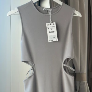 Grå klänning från Zara - Snygg grå ärmlös klänning från Zara med stilrena cut-out detaljer i sidorna. Perfekt för en modern och minimalistisk look. Klänningen har en enkel och elegant design som passar till många tillfällen. Aldrig använd! Köpt för 329:- 🩶