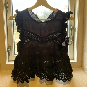 Svart blus från Zara - Säljer en jättefin svart blus från Zara med volangdetaljer och spets. Blusen är ärmlös och har en luftig design med broderade kanter.  Obs saknas en knapp i ryggen, se sista bilden🩷🩷