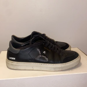 Svarta sneakers från Axel Arigato - Snygga svarta sneakers från Axel Arigato med vit sula och diskret logga på sidan. Skorna har snörning och en stilren design som passar perfekt till vardags. Tillverkade i skinn för en lyxig känsla.