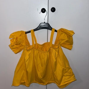 Gul topp från Zara kids - Säljer en söt gul topp från Zara kids med puffiga korta ärmar och axelband. Perfekt för sommardagar med sin ljusa och glada färg. Toppen har en luftig passform och är tillverkad i ett mjukt material.