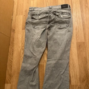 Grå jeans från Gina tricots - Snygga grå jeans från Gina trickot med bootcut-stil. De har en klassisk femficksdesign och knappar bak på fickorna. Perfekta för en avslappnad look.