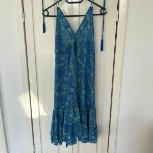 Miniklänning från italien - Snygg blågrön klänning med paisleymönster och volangdetaljer. Klänningen har en v-ringad öppen rygg och smala axelband som knyts⭐️ köpt i italien