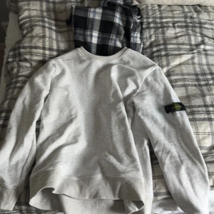 Grå sweatshirt från Stone Island - Säljer en stilren grå sweatshirt från Stone Island med deras ikoniska märke på ärmen. Tröjan har en rund hals och långa ärmar, perfekt för en avslappnad look. Passar bra till både jeans och joggers.