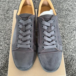 Grå sneakers från Christian Louboutin - Snygga grå sneakers från Christian Louboutin i mocka med den ikoniska röda sulan. Skorna har snörning och en stilren design som passar perfekt för en trendig look.