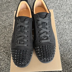 Svarta loubs - Snygga svarta sneakers i skinn från Christian Louboutin med coola nitar på tån. Skorna har en klassisk snörning och den ikoniska röda sulan. Perfekta för att ge din stil en edgy touch.