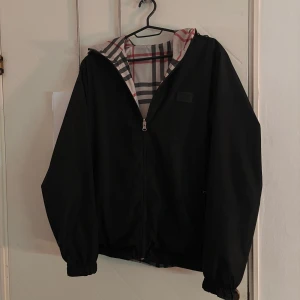 Svart vändbar burberry jacka  - Säljer en vändbar burberry jacka med svart utsida och rutig insida i beige, rött och svart. Jackan har dragkedja och långa ärmar, perfekt för höst och vår. Den rutiga sidan ger en klassisk look medan den svarta sidan är mer diskret. Det finns ett litet hål på framsidan av den svarta sidan men inget som syns jättemycket, pris kan diskuteras!