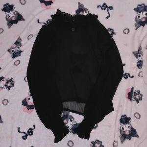 Svart blus med volangdetaljer -  svart lolita blus med volangdetaljer vid halsen och ärmsluten. Blusen har långa ärmar och en lätt transparent design som ger en elegant look. Kopt från Devilinspired. Perfekt för svalare sommar coords. 