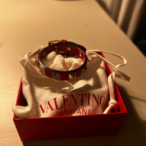 Rött Valentinoarmband - Snyggt rött armband från Valentino. Armbandet har en justerbar rem och kommer i med dustbag. Den är i så bra skick, men kommer tyvär inte till användning längre