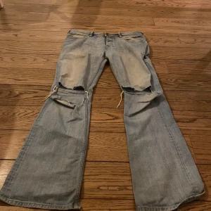 Blå jeans från Diesel - Säljer ett par blå jeans från Diesel med slitna detaljer vid knäna. Byxorna har en bootcut-stil och klassisk femficksdesign. Perfekta för en avslappnad look.