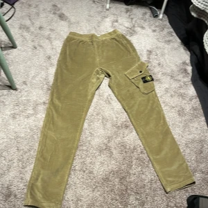 Manchester byxa ifrån stone island använd en gång, size 14 passar folk som är tretton och femton. Ny pris är 2000 vad jag har sett men jag är uppe för att prata om annat pris  - Snygga beige manchesterbyxor från Stone Island med en cool cargoficka på sidan. Byxorna har en elastisk midja för extra komfort och en broderad logga på fickan. Perfekta för en avslappnad stil med en touch av lyx.