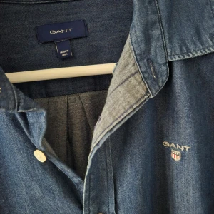 Jeansskjorta GANT - Snygg blå jeansskjorta från GANT med klassisk krage och knappar framtill. Skjortan har långa ärmar och en liten broderad logotyp på bröstet. Perfekt för en avslappnad stil. Nypris 1599:-