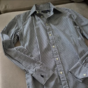 Randig skjorta Polo Ralph Lauren - Snygg och stilren svartvit randig skjorta från Polo Ralph Lauren. Skjortan har långa ärmar och knappar framtill. Perfekt för en klassisk look. Nypris 2199:-