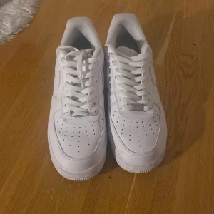 Nike Air Force  - Snygga och klassiska vita Nike Air Force sneakers med snörning. Perfekta för en stilren look. Skorna har en ikonisk design med perforerade detaljer på ovansidan för ventilation.