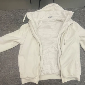 Vit jacka med huva från Max Fashion - Säljer en stilren vit jacka med huva från Max. Jackan har dragkedja framtill och är långärmad. Perfekt för kyligare dagar med sin quiltade insida som håller värmen. Enkel och snygg design som passar till det mesta. Jackan är endast användad nån enstaka gång och finns inte längre kvar i sortiment någonstans i hela världen. Jackan är köpt från dubai och är en garanterad conpliment getter. Den funkar för alla väder och alla tillfällen.