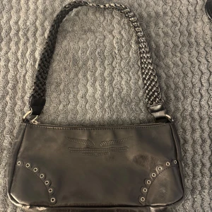 Svart axelväska med flätat axelband - Snygg svart axelväska i skinn med ett coolt flätat axelband. 