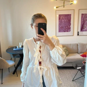 Vit overshirt med knytband - Säljer en vit overshirt med puffiga axlar och långa ärmar. Blusen har flera knytband framtill och en lätt, luftig känsla.  Den är onesize men tror den passar perfekt på s-m då den är lite stor för mig som normalt har xs.