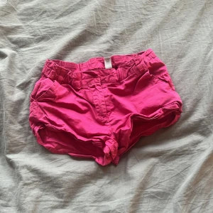 Knallrosa shorts med fickor - Snygga knallrosa shorts med normal passform och praktiska fickor på sidorna. De har bälteshällor och stängs med knapp och dragkedja. Perfekta för varma sommardagar och riktigt bekväma att ha på sig.
