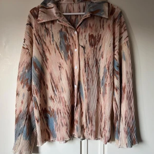 Aprikos mönstrad manchester-skjorta - Säljer en oversized skjorta i beige manchester med unikt abstrakt mönster i blått och brunt. Skjortan har långa ärmar, klassisk krage och knäppning framtill. Materialet är ribbat och ger en cool struktur. Perfekt för dig som gillar statement-plagg.