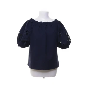 Mörkblå blus med puffärm By Malina - Supersnygg mörkblå blus från By Malina med offshoulder-modell och puffiga korta ärmar. Ärmarna har broderade blommor och paljettdetaljer som ger extra wow-känsla. Perfekt för dig som vill sticka ut lite extra med en trendig och luftig topp.