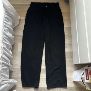 Svarta mjukisbyxor med snörning - Svarta mjukisbyxor med bred resår och snörning i midjan. Byxorna har raka ben, stora fickor fram och bak samt är gjorda i mjukt bomullsmaterial. Perfekta för chill dagar eller när du vill vara bekväm men ändå se stilren ut.