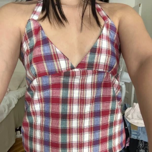 Rutig halterneck topp - Supersöt rutig linnetopp med halterneck och knyt i nacken. Toppen har röd, vit, blå och grön färg i rutigt mönster och v-ringad front. Perfekt till jeans eller kjol för en chill sommarlook. PS. Handsydd av vintagetyg – unik design, ej fast fashion.