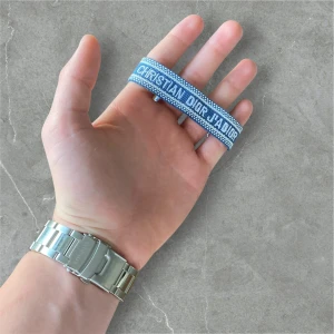 Blått armband från Christian Dior - Snyggt blått armband från Christian Dior med texten 'Christian Dior J'Adior' broderad i vitt. Armbandet har en vävd struktur och justerbar knytning för perfekt passform. Perfekt accessoar för att lyfta din outfit.