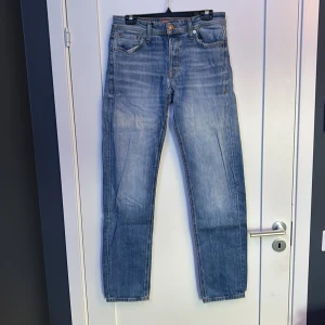 Blå jeans Jack & Jones Comfort Mike - Snygga blå jeans från Jack & Jones, modell Comfort Mike. Jeansen har klassisk femficksdesign, raka ben och orangea kontrastsömmar. Materialet är slitstarkt denim i bomull och passformen är relaxed och bekväm. Perfekta för en chill och avslappnad stil.