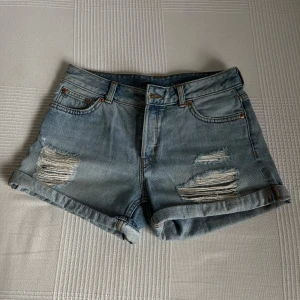 Ljusa jeansshorts från Monki - Jeansshorts från Monki. Shortsen är i en ljusare blå tvätt med slitningar framtill. Shortsen har 4 knappar framtill. 