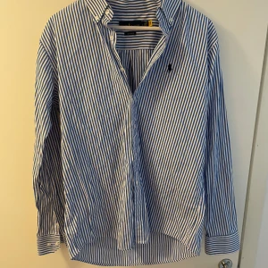Polo Ralph Lauren skjorta  - Vit blå randig skjorta från Poli Ralph Lauren, perfekt till sommaren! Storlek L                                         Säljes då den va för stor.                                              Nypris 1200kr mitt pris 199kr