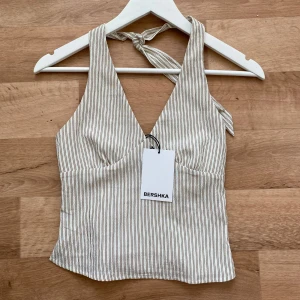 Randig linnetopp från Bershka - Superfin randig linnetopp från Bershka i beige och brunt. Toppen har v-ringning, knyt i nacken och smockad rygg för extra komfort. Perfekt croppad längd och tunn, luftig känsla – ett måste för varma dagar! Helt ny💕Slutsåld på hemsidan. 