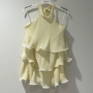 Dress engla från Missay - Superfin ljus kortklänning med flera lager volanger och plisserat tyg. Har inte alls används är helt ny. Klänningen har halterneck med knyt i nacken och är ärmlös. Perfekt för sommarens alla tillfällen när du vill känna dig extra söt och trendig.