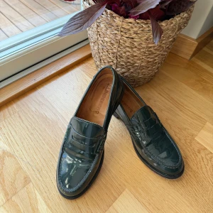 Mörkgröna lackloafers från J.Lindeberg - •Snygga och bekväma mörkgröna loafers från J.Lindeberg i glansigt lackat skinn.  •Klassisk penny loafer-modell med rund tå och diskreta sömmar.  •Perfekta för dig som vill ha en stilren och trendig look med lite extra edge. •Mycket bra skick. Sparsamt använda. •Material: läder •Storler: 37 •Ordinarie pris: 2600 kr. Djurfritt och rökfritt hem.