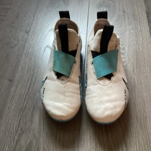 Nike Mercurial Zoom fotbollsskor vita/blå - Nike Mercurial Zoom fotbollsskor i vitt med blå och svarta detaljer. Skorna har elastiskt band över vristen, dragflikar fram och bak samt mönstrad sula för bra grepp. Snygg design med stora Swoosh-loggor och coola blå accenter på sidorna.