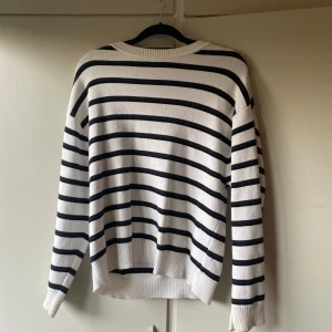 Vit och svart randig stickad tröja - Snygg stickad tröja i vitt med svarta horisontella ränder. Tröjan har rund halsringning, långa ärmar och ribbade muddar vid ärmslut och nederkant. Perfekt för en chill och stilren look.