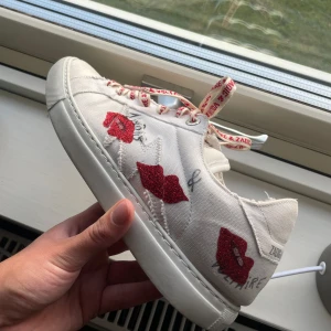 Zadig & Voltaire vita sneakers med röda detaljer - Snygga vita sneakers från Zadig & Voltaire med röda snören med logga och röda läppar på sidorna. Skorna har rund tå, platt sula och är tillverkade i tyg. Kartong medföljer. Användt skick🥰